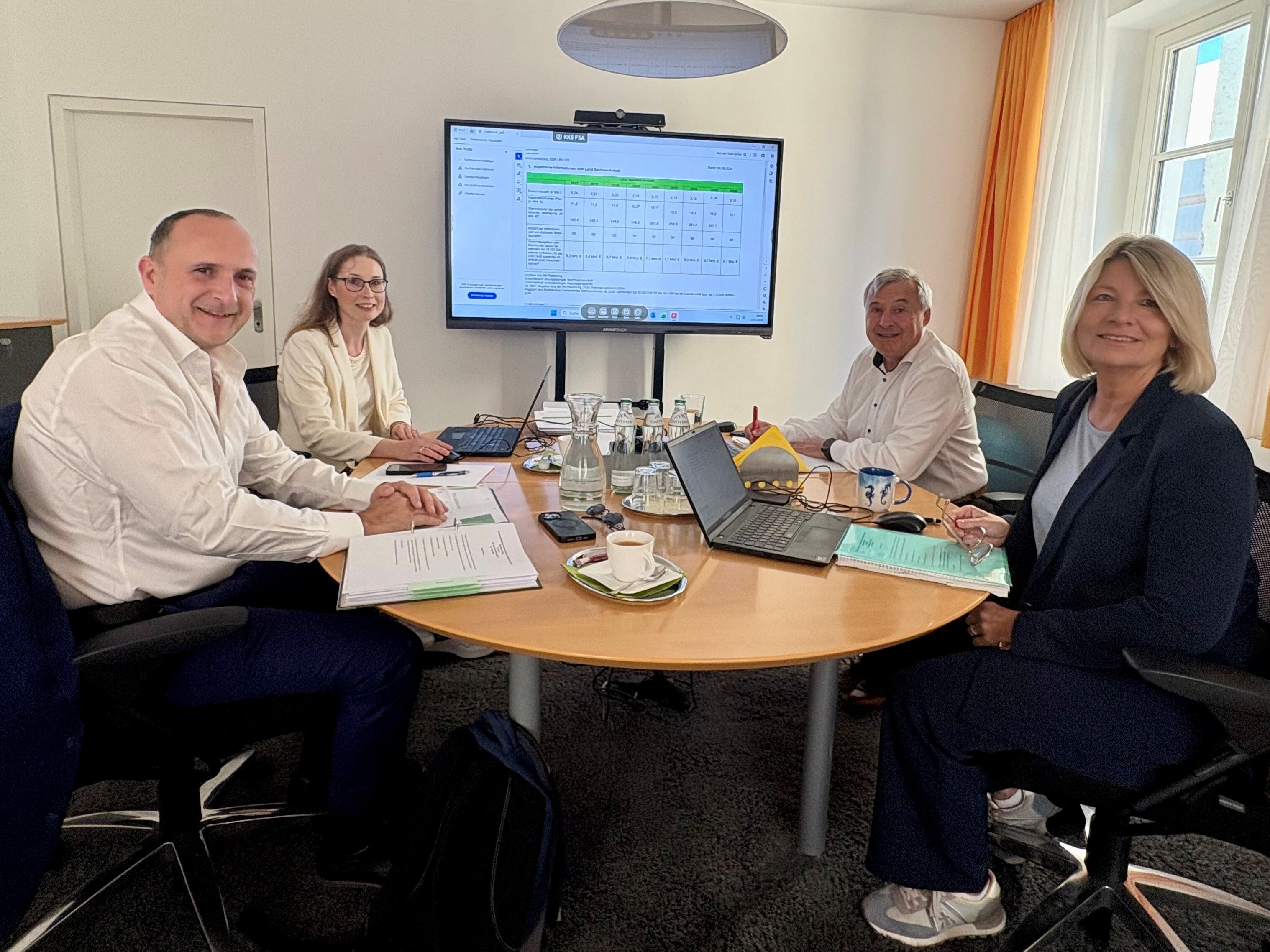 Vier Personen sitzen am Tisch in einem Büro